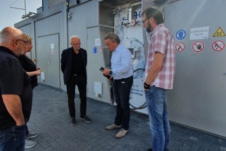 Vier Personen lassen sich vor einer technischen Anlage im Außenbereich ein technisches Gerät erläutern