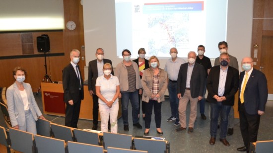13 Personen stehen mit Mund-Nasen-Schutz in einem Hörsaal vor einer Leinwand